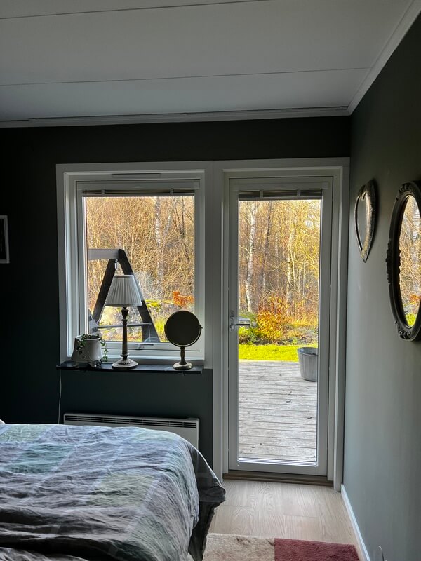 Nyinstallerade fönster med vita karmar och utsikt mot höstträdgård i mörkt sovrum