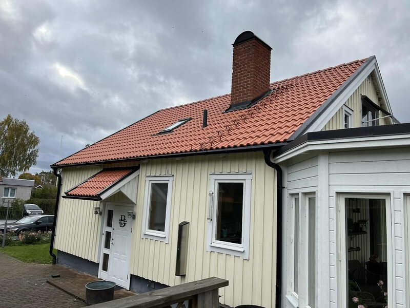 Ljusgul trävilla med orangeröda takpannor, tegelskorsten och takfönster