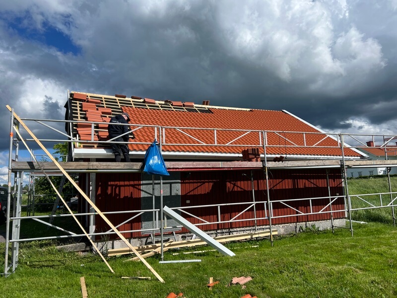 Rödmålat trähus med byggställning runt om medan takläggare tar bort gamla röda takpannor