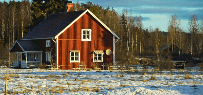 Rött trähus med vita knutar omgivet av snötäckt mark och skog