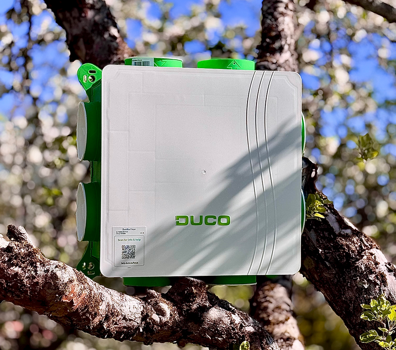 Duco ventilationsaggregat i vitt och grönt, fotomontage bland trädgrenar