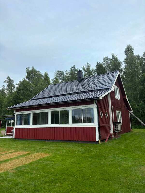 Rödmålad villa med nylagt mörkt plåttak och inglasad veranda med vita fönsterfoder
