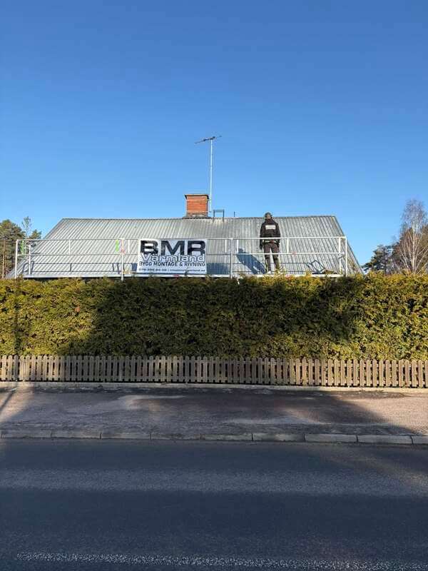 Hus med ställning längs takfoten och BMR Värmlands skylt, sett från gatan bakom häck