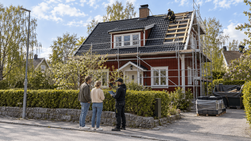 Takläggare går igenom en pågående takrenovering med ett par framför en röd trävilla.