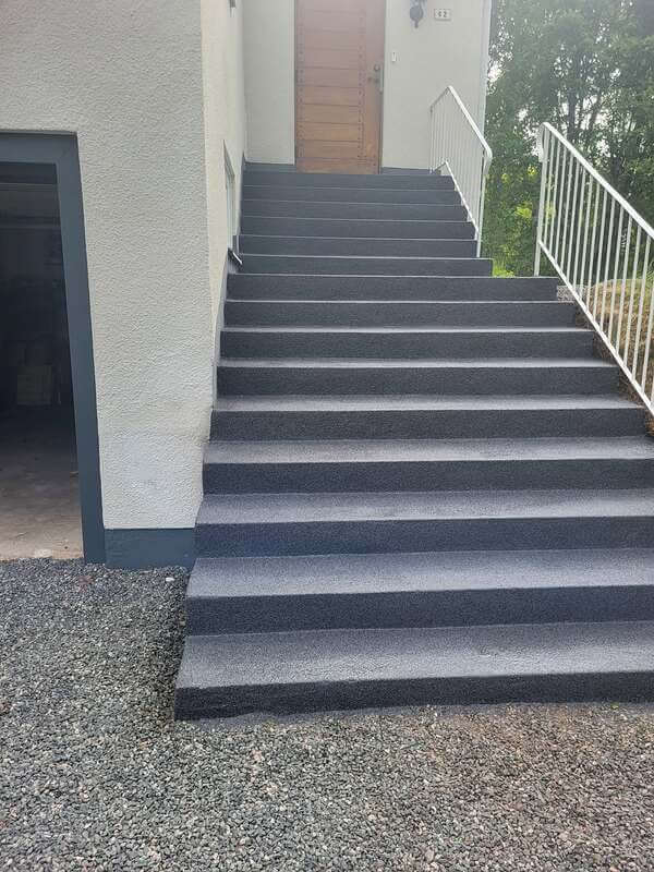 längre betongtrapp i mörkgrå färg till vitt putsat hus