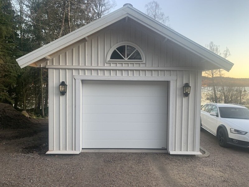 Vitt garage med vit takskjutport och halvrunt fönster i gaveln, sett snett framifrån