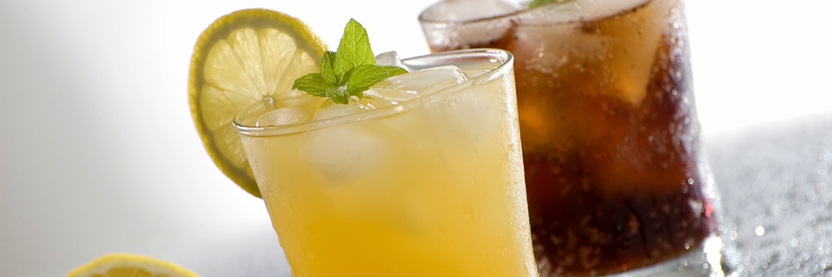 A glass of soda with ice and a yellow cocktail served with ice and lime 