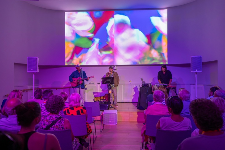 Guests sat in a theatre-style setup, facing the guest speakers on stage. The room has pink uplighters and there is a large screen at the front of the room