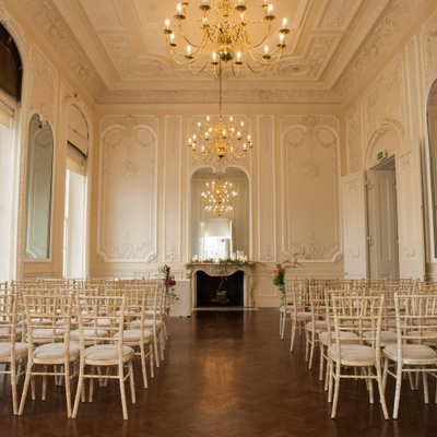 Wedding chairs set up theatre style for a wedding ceremony in grand room with elegant gold chandeliers hanging from the ceiling