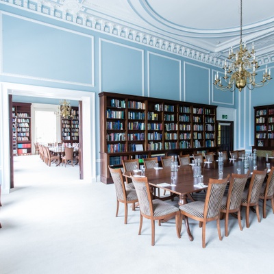 Two large rooms with bookselves and a long wooden boardroom table with chairs, notepads at each place setting and bottles of water on the table