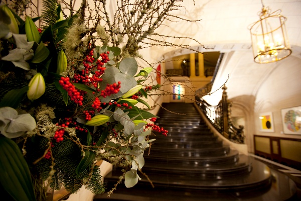 A close up of a floral arrangement with red and green foliage, and the staircase in the background