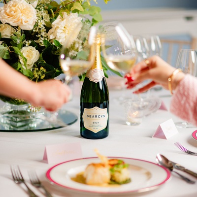 Two glasses cheering, a plate with a fish course and a bottle of Searcys Champagne