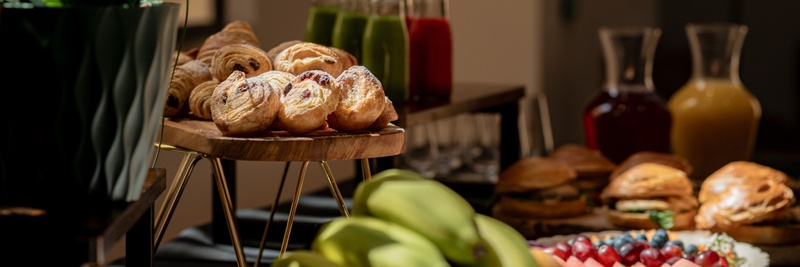 A croissant, strawberry jam spread out on a small round plate with small square-cut pieces of butter and small jam jars laid on the side