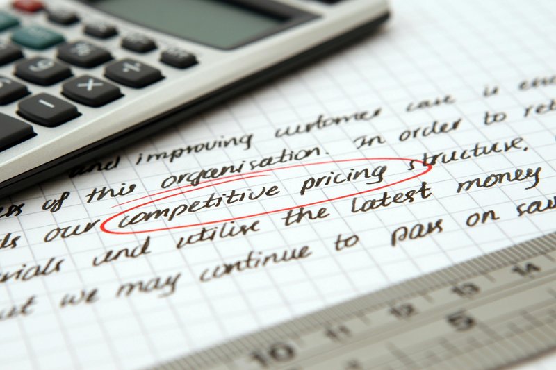 A calculator placed on graph paper contain text with the words competitive pricing circled.