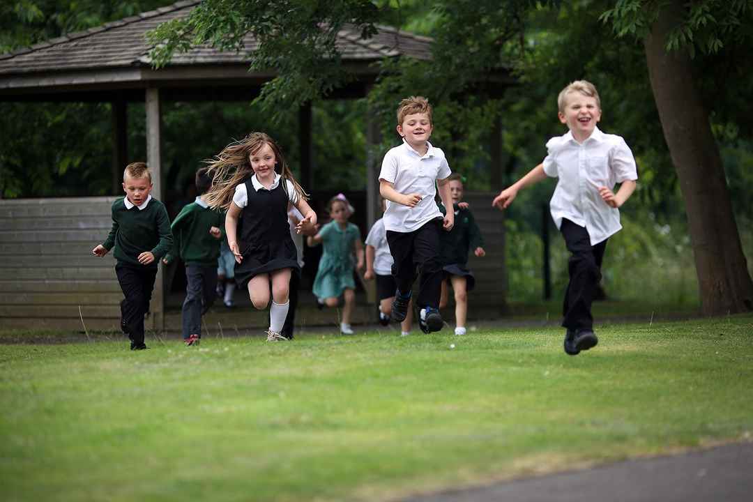 Several school children running and having fun on grass