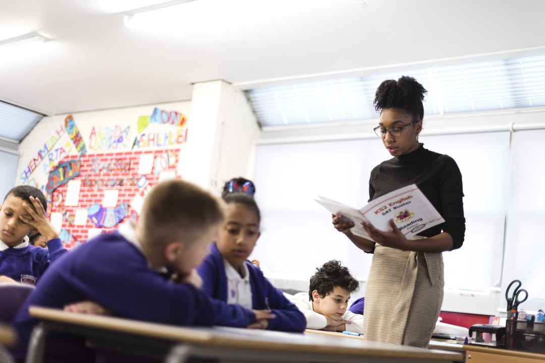 Teacher reading from workbook in front of pupils