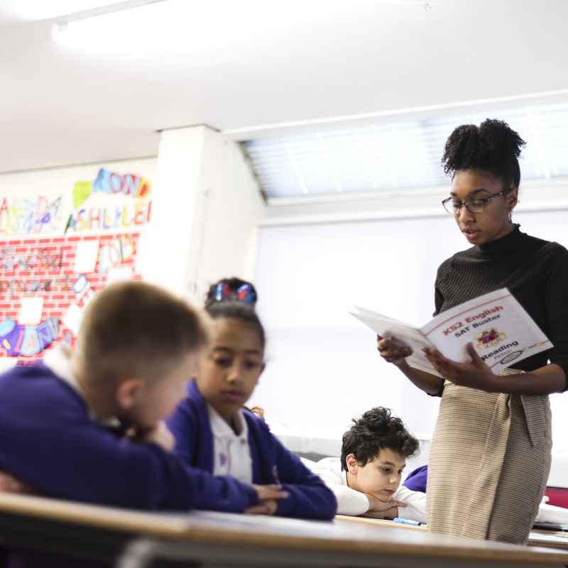 Teacher reading from workbook in front of pupils