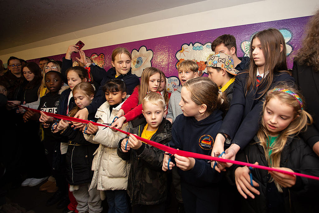 Group of school children all getting ready to cut a long ribbon with scissors