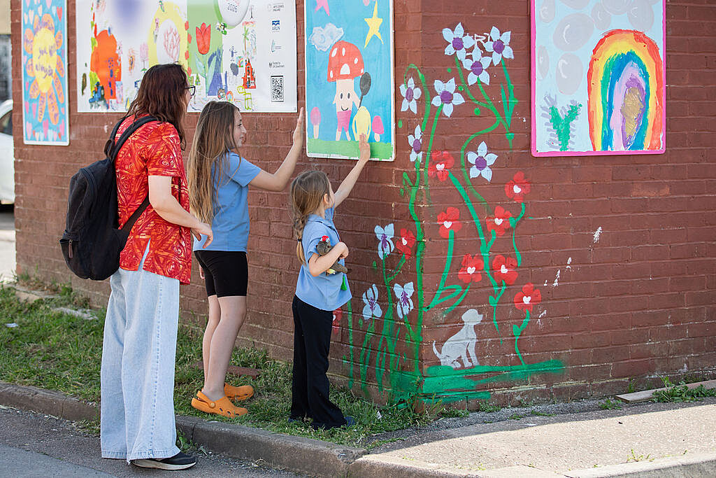 Two primary school age girls pointing at children's artwork on a brick wall, showing an adult that is with them