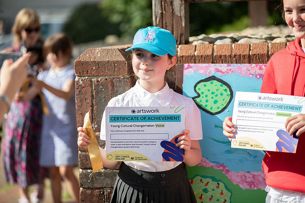 Young girl in primary school uniform smiling holding a certificate for youth voice