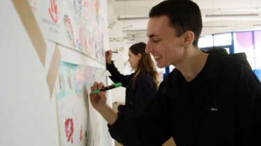 A young man and woman draw on paper that is stuck to a wall