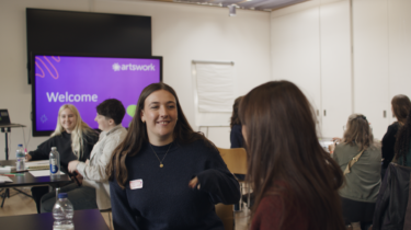 Young consultants sit in a room with an Artswork presentation on a screen behind them.