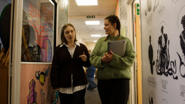 A young woman walks beside a mentor with a laptop in her hand