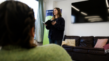 A young woman stands and reads poetry from a book