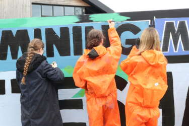 Three young people painting a mural designed to represent Dover's mining history with green and blue paint