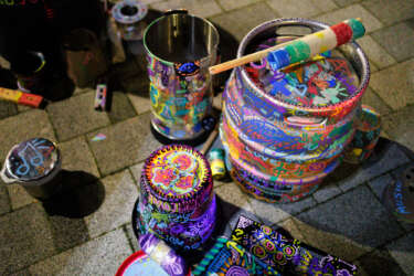 A pile of instruments made from recycled materials as part of a 'Junk Band'. The surfaces of drums, shakers, and cymbals have been covered in colourful doodles by young people.