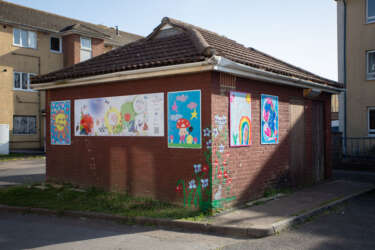 brick outbuilding with decorated panels attached which contain colourful children's drawings