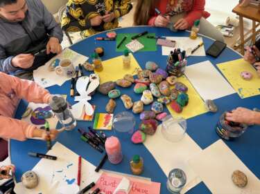 Children and their families sit round a table painting rocks with bright colour paints.