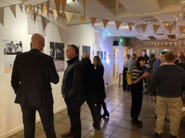 people gathered at private exhibition view with bunting and photographs displayed on wall in background