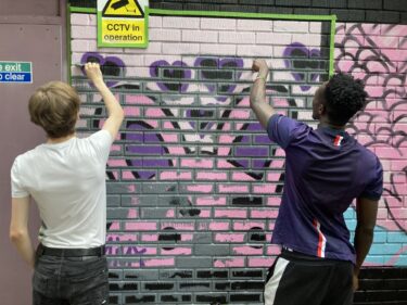Two young people spray painting a mural of hearts onto a wall