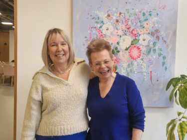 Annabel (left) and Louise (right) stand and smile in front of a floral work of art