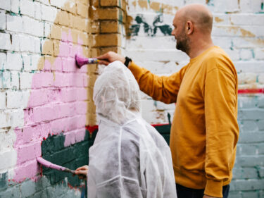 An adult and young person painting a section of a mural together
