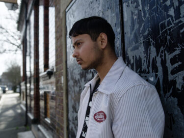 A young man leans on a doorway looking glum.