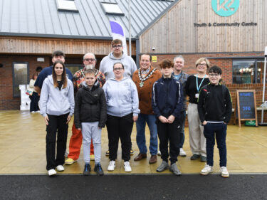 A group of young people, an artist and local town councillors stood in front of a new community centre they helped open together
