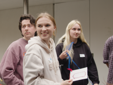 4 young people in casual clothing in a candid shot, person at forefront smiling at something off camera
