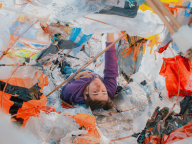 Young person laying inside the large whale sculpture they helped make out of plastic waste