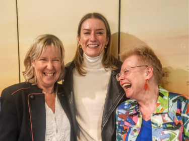 Our Co-CEO's Annabel and Louise stand either side of Katie Jackson - everyone is laughing joyfully.