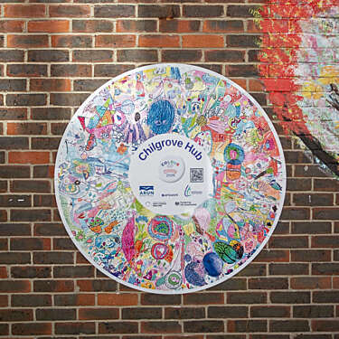 A large circular plaque decorated with lots of layered children's drawings, attached to a brick wall