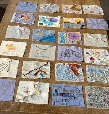 Fabric panels with different pictures drawn and embroidered onto them laid out on a table