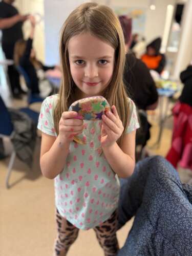 A young girl holds a painted rock in her hands.