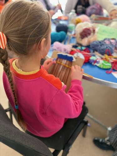 A young girl is sitting on a chair doing some weaving with fabrics.