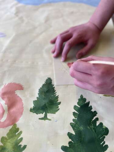 hands using a stencil to paint something onto a piece of paper with trees