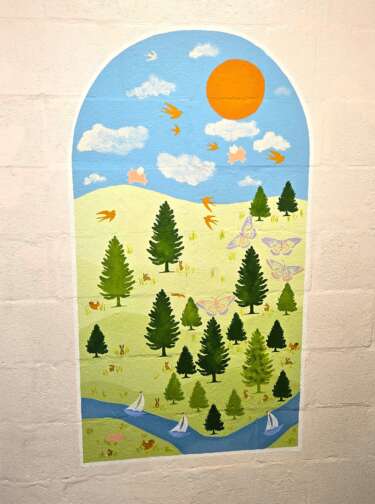 An arch shaped mural depicting a sunny countryside scene with birds, butterflies, trees, and river with sailboats, painted onto a plain wall