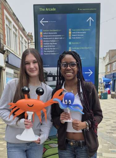 2 young people pose for the camera holding the 3D printed models of sea creatures.