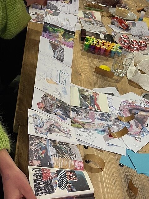 A young person is holding an open hand-crafted zine with collages from each member of the Youth Board. On the table are various collage materials, stamps, and paper.
