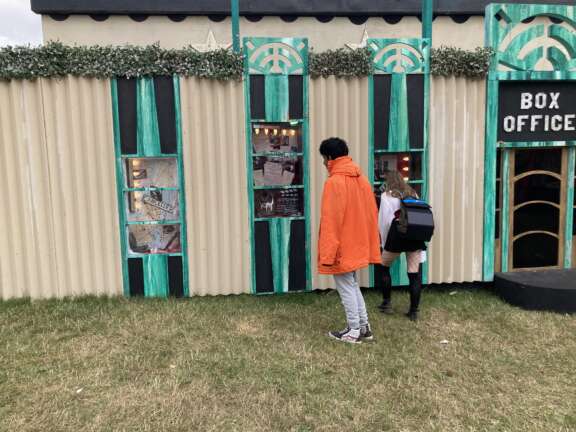 Two young people are exploring the three-piece window installation that they have just created at Boomtown Festival. They are staring into the windows looking at pieces of script, photos, and newspaper headlines.
